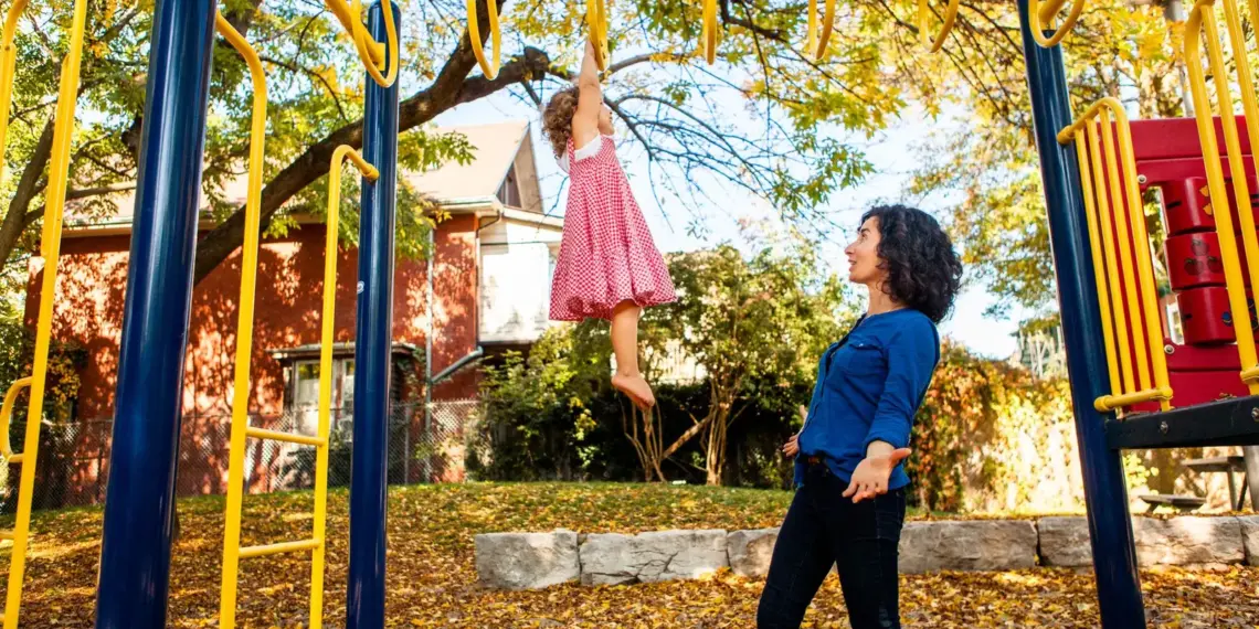 Mother helping a young child climb at a Toronto playground in autumn