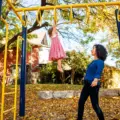 Mother helping a young child climb at a Toronto playground in autumn
