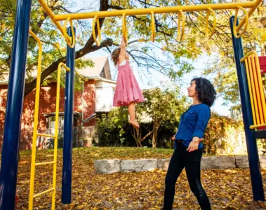 Mother helping a young child climb at a Toronto playground in autumn