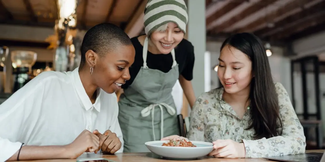 Three women sharing a meal with a restaurant worker at their table
