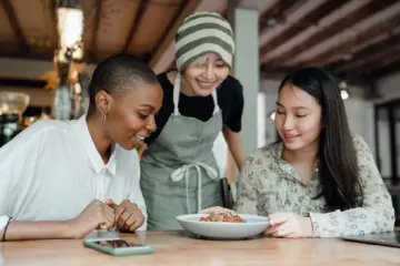 Three women sharing a meal with a restaurant worker at their table