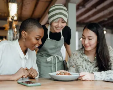 Three women sharing a meal with a restaurant worker at their table
