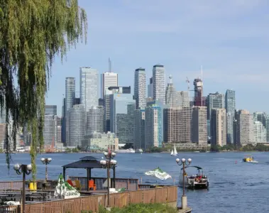 Toronto skyline across the harbour with boats, trees and outdoor seating in the foreground