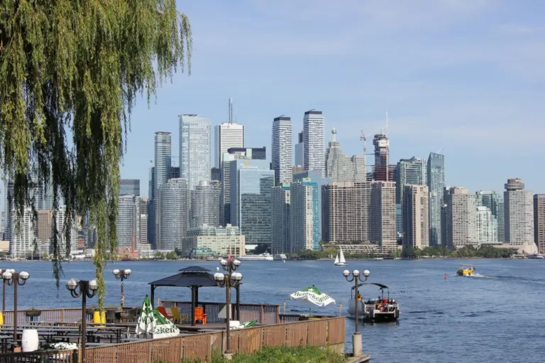 Toronto skyline across the harbour with boats, trees and outdoor seating in the foreground