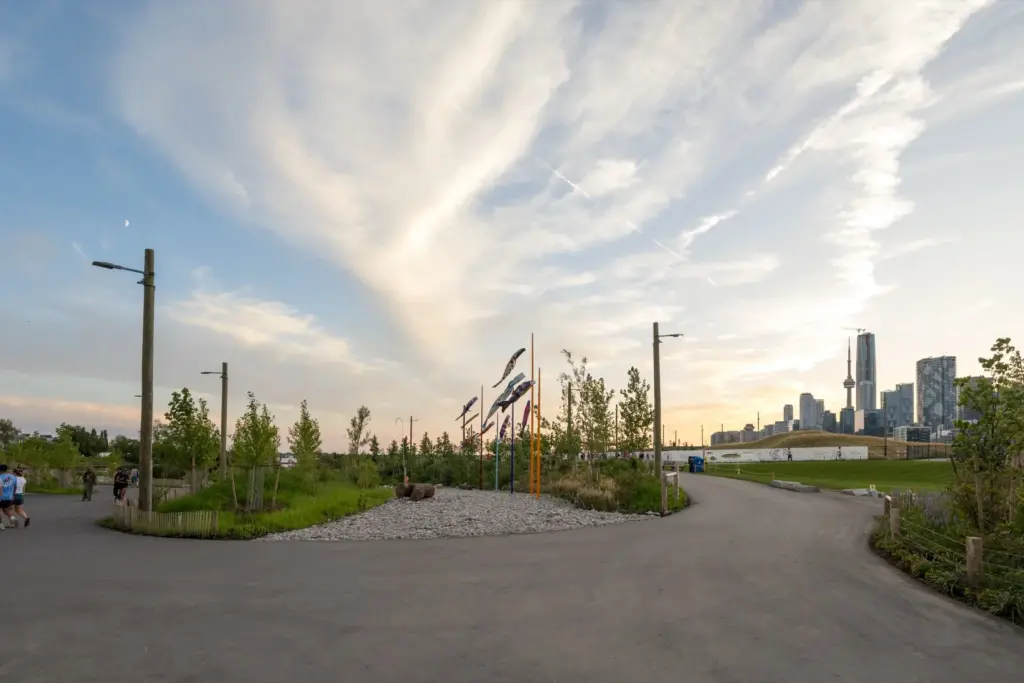 Paths, plantings, public art and the Toronto skyline at Biidaasige Park near sunset