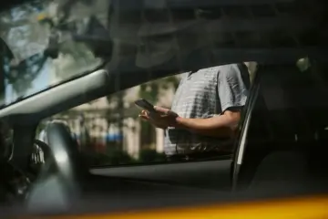 Person checking a smartphone beside a car while waiting for a ride