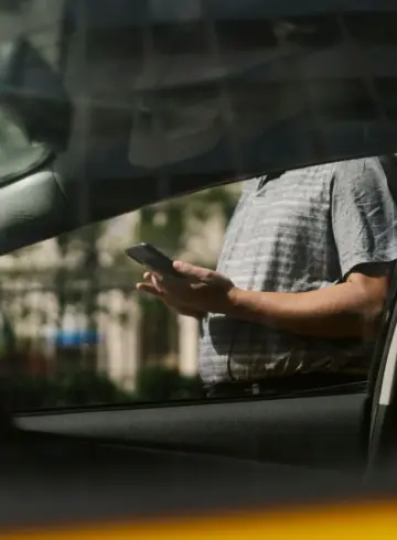 Person checking a smartphone beside a car while waiting for a ride