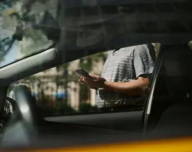 Person checking a smartphone beside a car while waiting for a ride