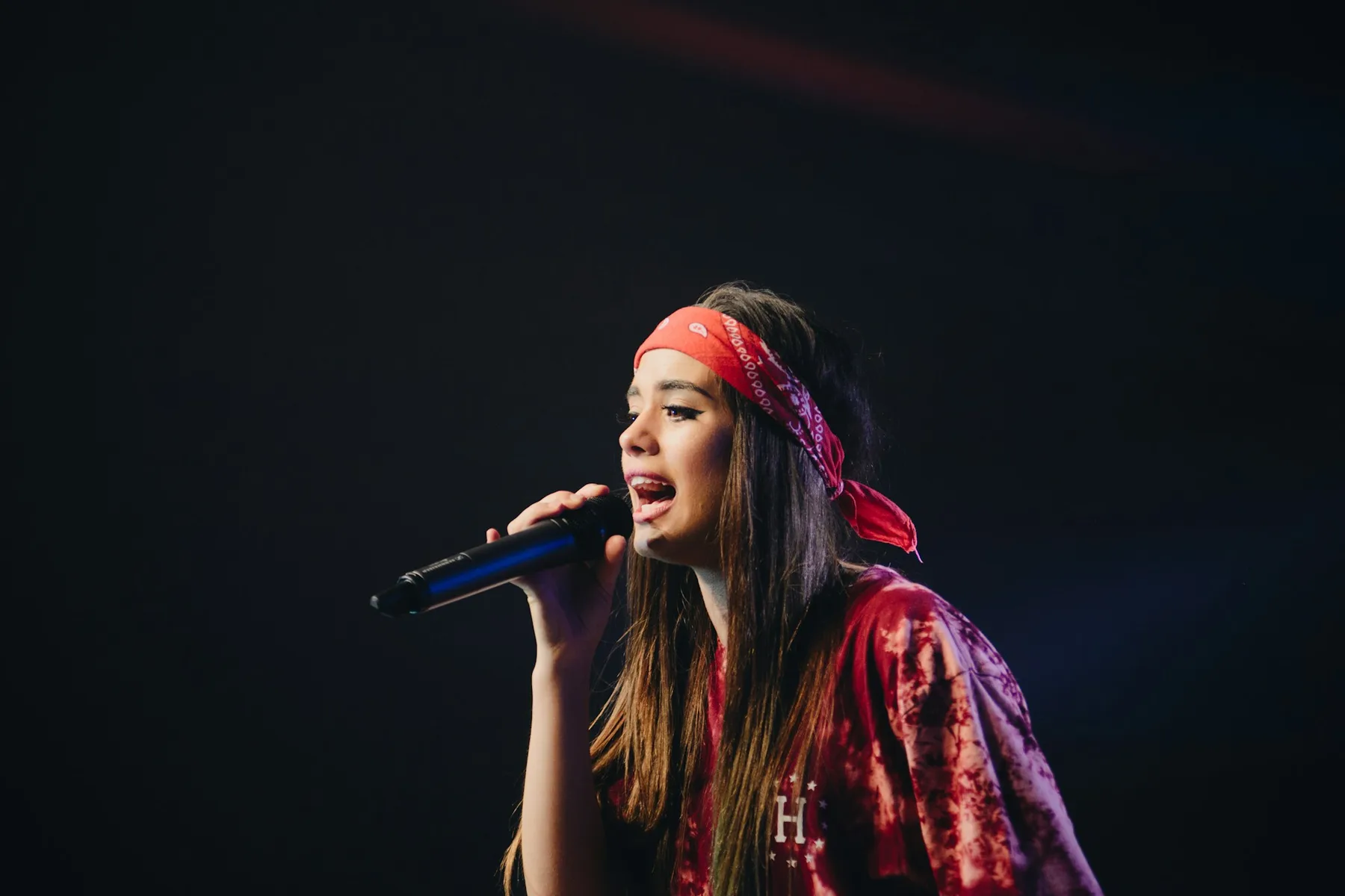 A woman sings into a microphone on a dark stage