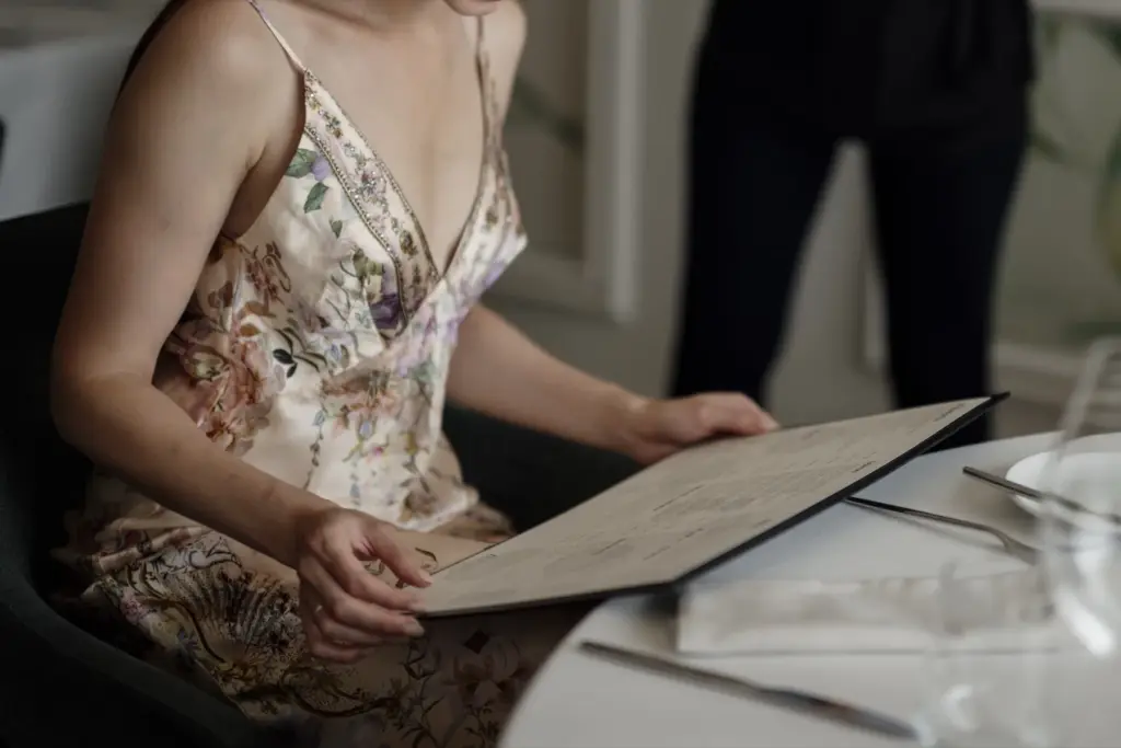 Woman seated at a restaurant table while reading a large menu