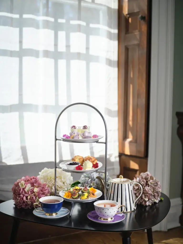 A tiered stand of scones, colourful savouries and sweets with teacups and flowers at the AGO