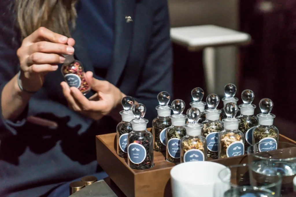 A server offering small jars of tea for a guest to smell at Astor Lounge