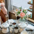 A woman with a teacup beside flowers and a tiered afternoon tea stand at Astor Lounge