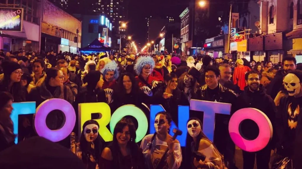Costumed Halloween visitors holding large Toronto letters on Church Street