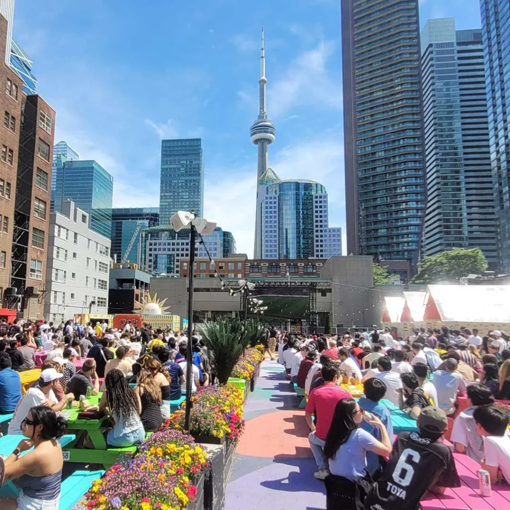 Picnic tables and an outdoor sports screen at RendezViews with the CN Tower beyond