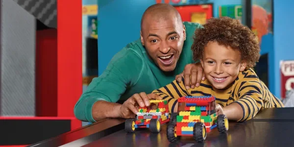 An adult and child building a small wheeled LEGO model