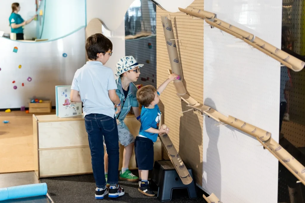 Children testing a wall-mounted ball run with an adult