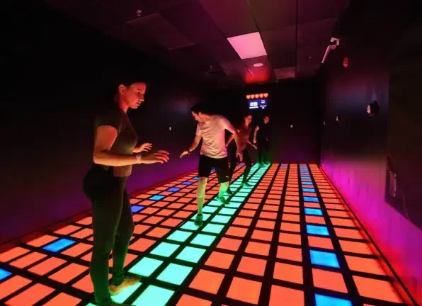 Two players crossing a floor of coloured light-up tiles at Activate
