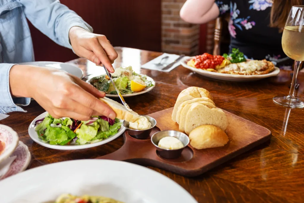 People serving salad and bread beside plates of pasta