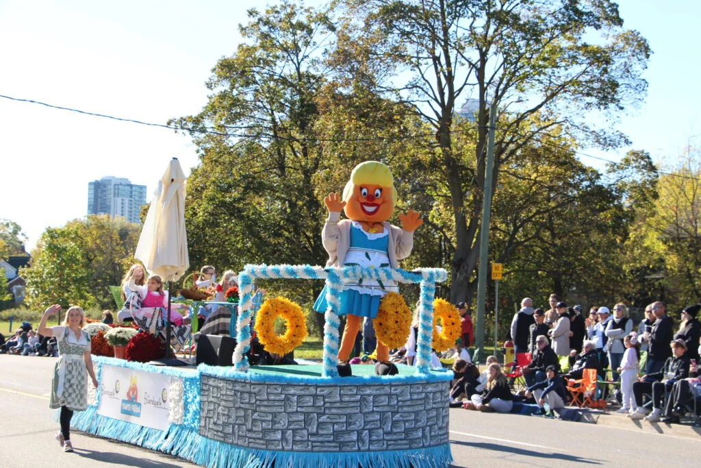 An Oktoberfest parade float passing families along a tree-lined street