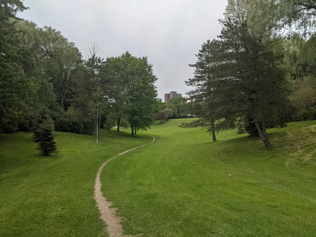 A paved path and mature trees in Dallington Park in Toronto