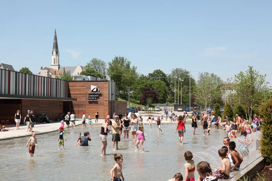 People near the summer water feature at Newmarket’s Riverwalk Commons