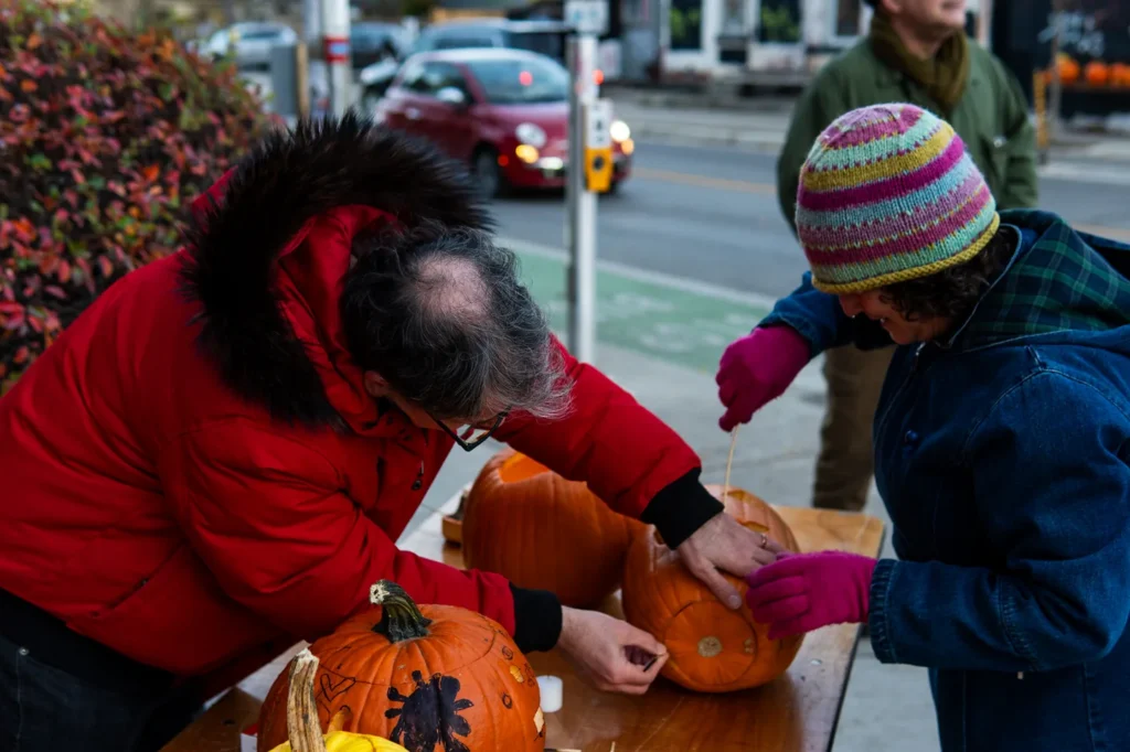 An adult and a child arranging pumpkins on a table along Harbord Street