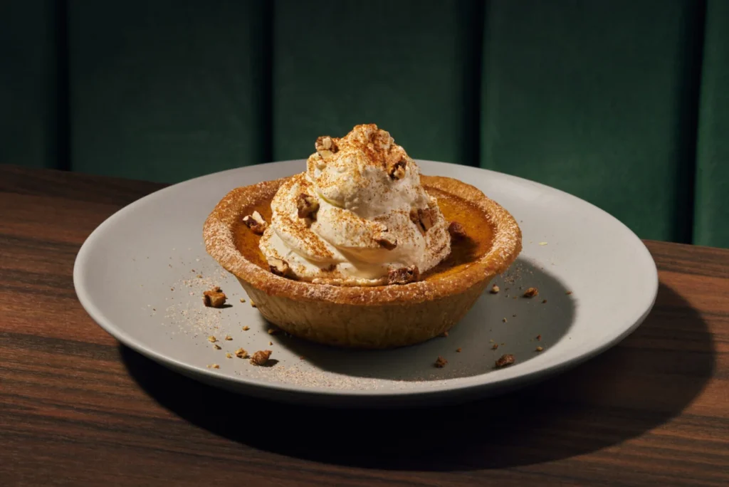 A small pumpkin pie topped with cream on an Earls plate