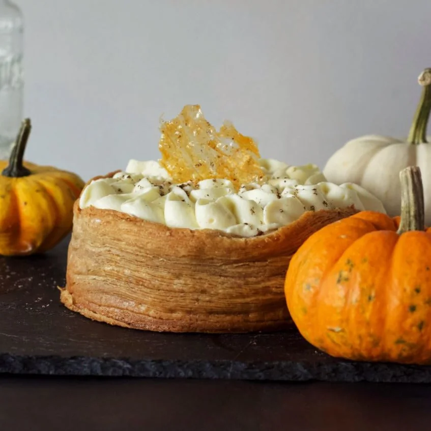 A tall pumpkin pie topped with cream and pastry leaves
