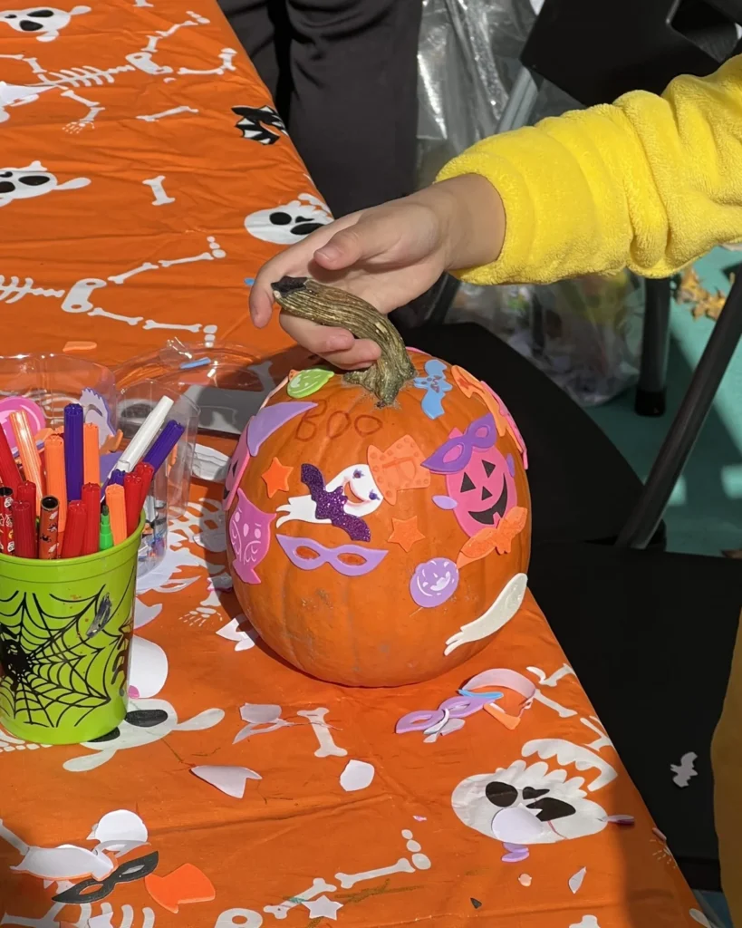 A child decorating a small pumpkin with colourful paint