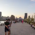 People sitting and walking along Water's Edge Promenade at Biidaasige Park at sunset