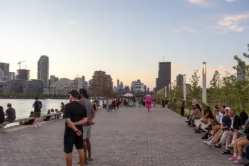 People sitting and walking along Water's Edge Promenade at Biidaasige Park at sunset