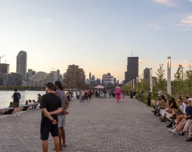 People sitting and walking along Water's Edge Promenade at Biidaasige Park at sunset