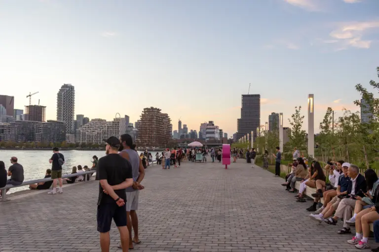 People sitting and walking along Water's Edge Promenade at Biidaasige Park at sunset
