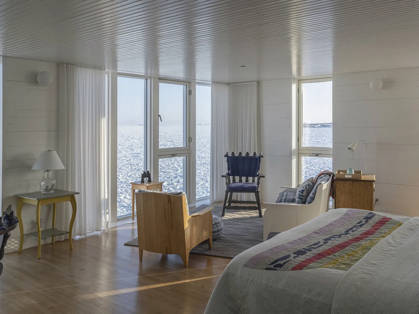 Quilts, wooden chairs and large ocean-facing windows in a Fogo Island Inn guest room