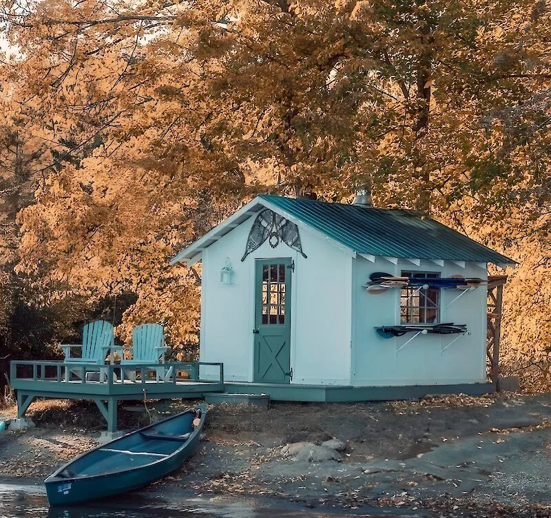 A blue lakeside boathouse and canoe surrounded by autumn leaves at Manoir Hovey