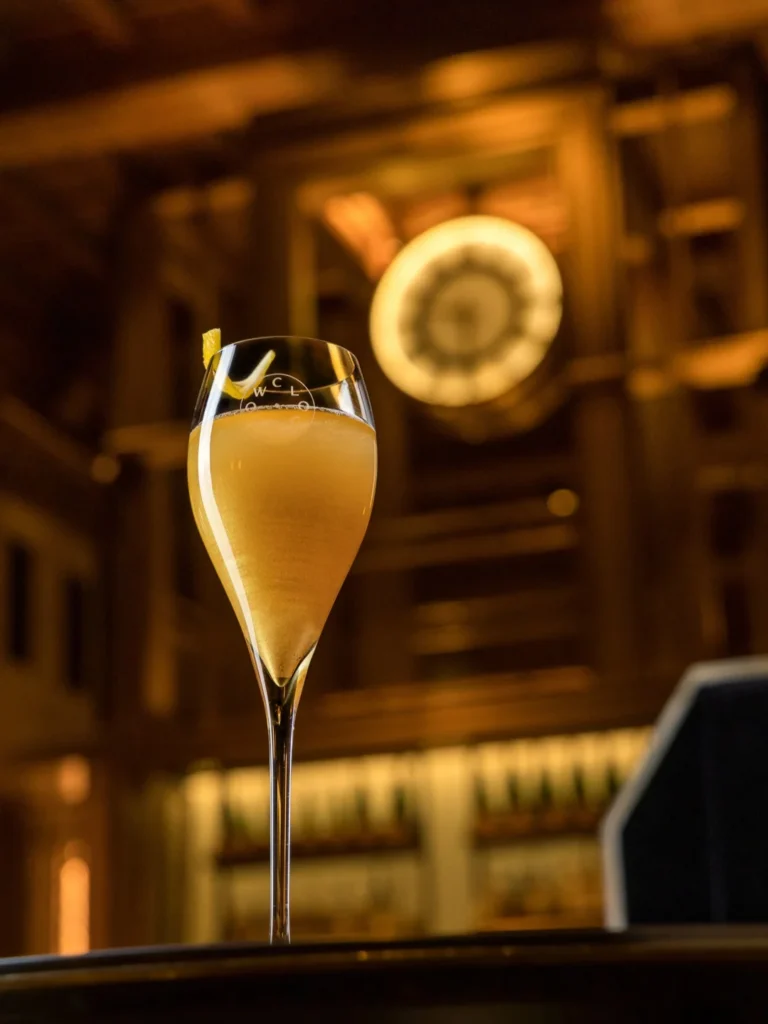 A golden cocktail in a tall glass with the CLOCKWORK clock in the background