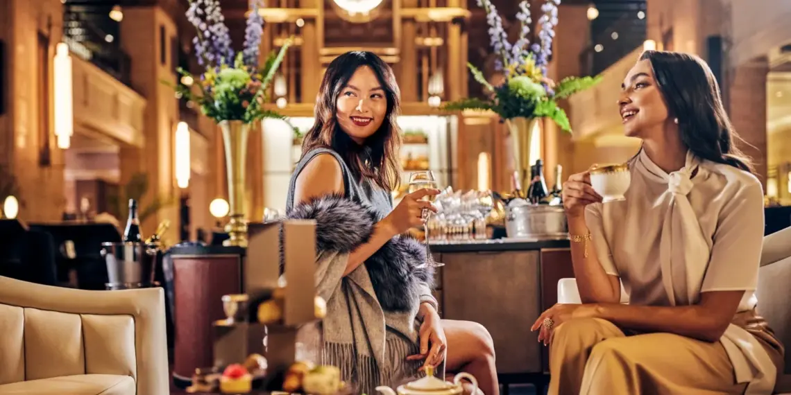 Two women sharing afternoon tea beneath the clock at Fairmont Royal York