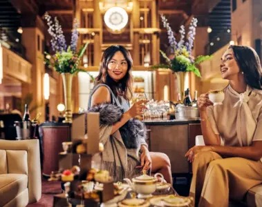 Two women sharing afternoon tea beneath the clock at Fairmont Royal York