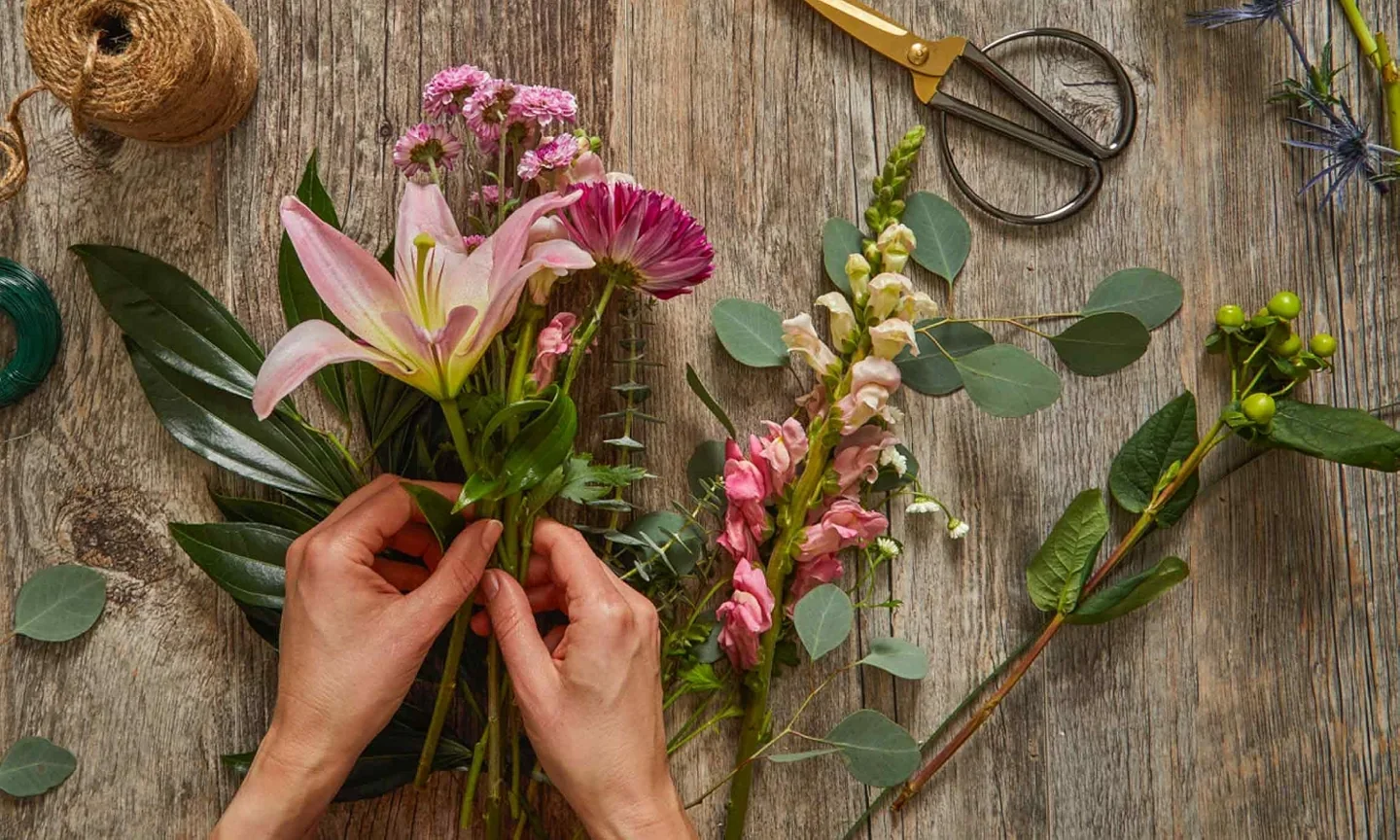Hands arranging cut flowers on a wooden work surface