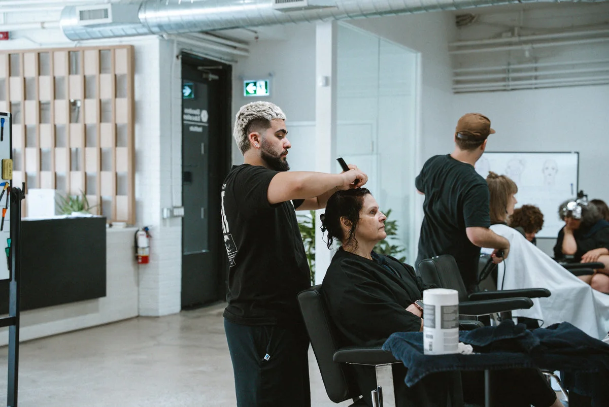 A stylist cutting a seated client's hair in a training salon.