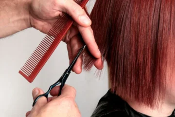 Scissors trimming a straight red bob at chin length.