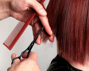 Scissors trimming a straight red bob at chin length.