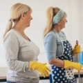 Two cleaners in gloves holding a caddy of cleaning supplies.