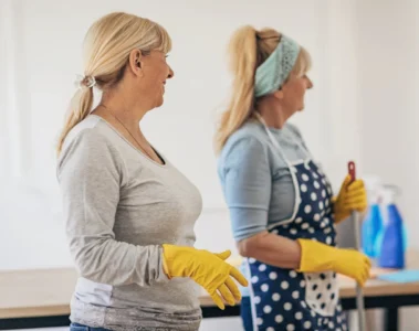 Two cleaners in gloves holding a caddy of cleaning supplies.
