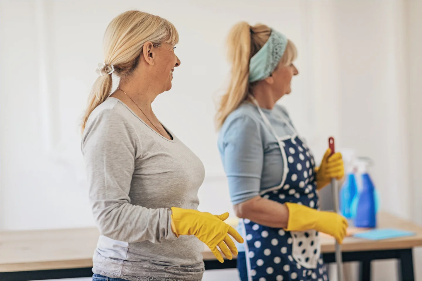 Two cleaners in gloves holding a caddy of cleaning supplies.