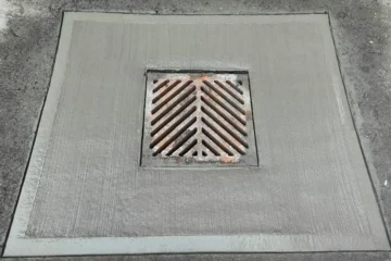 A metal catch-basin grate set into a concrete surround