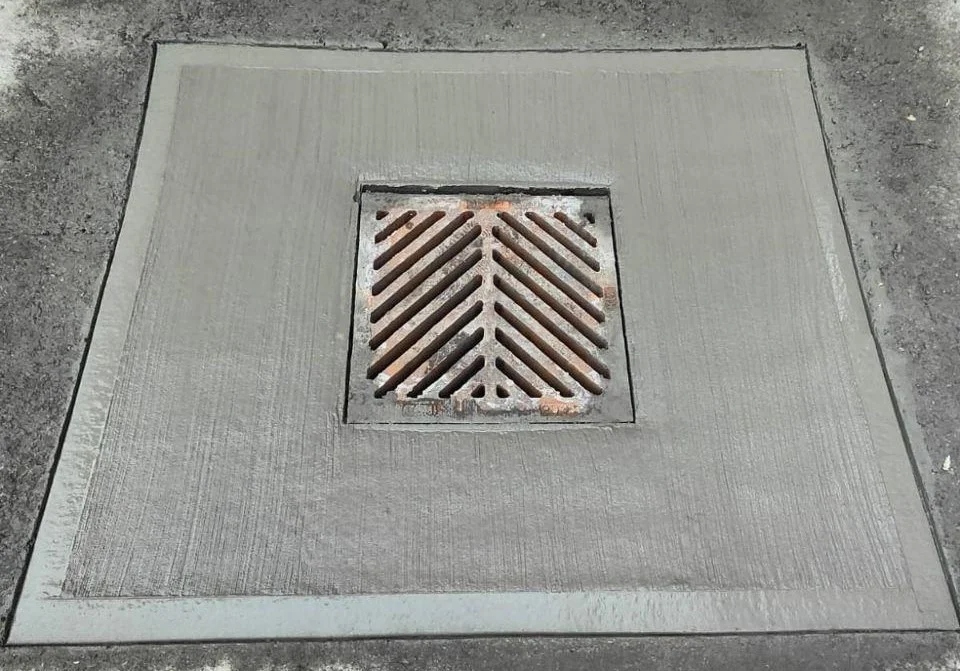 A metal catch-basin grate set into a concrete surround
