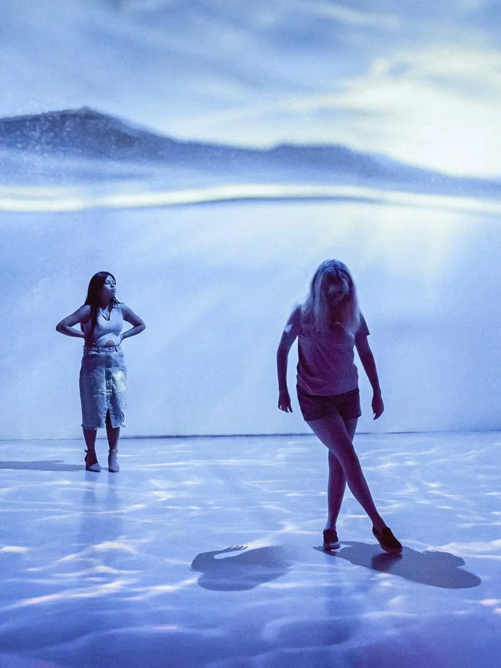 Two visitors in a room with floor and wall projections