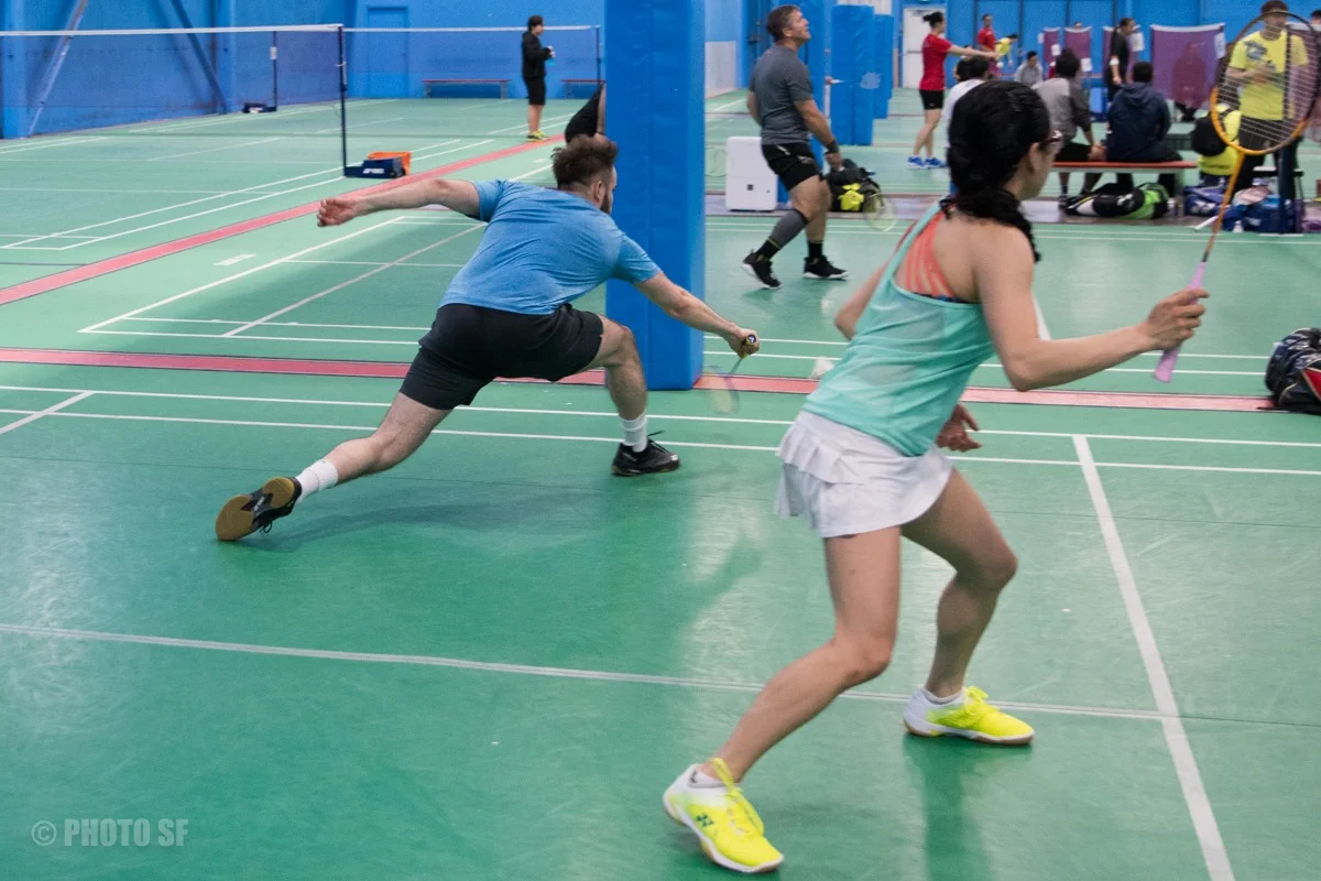Two players moving across a badminton court at Epic Sports